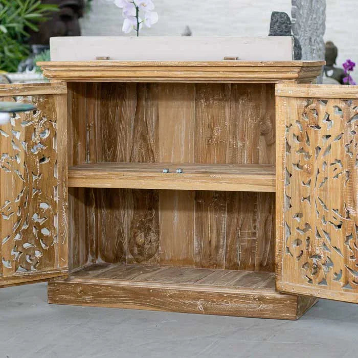 Detalhe da frente da estante de madeira balinesa com entalhes florais e pátina esverdeada, mostrando a riqueza do trabalho artesanal e o estilo étnico elegante.