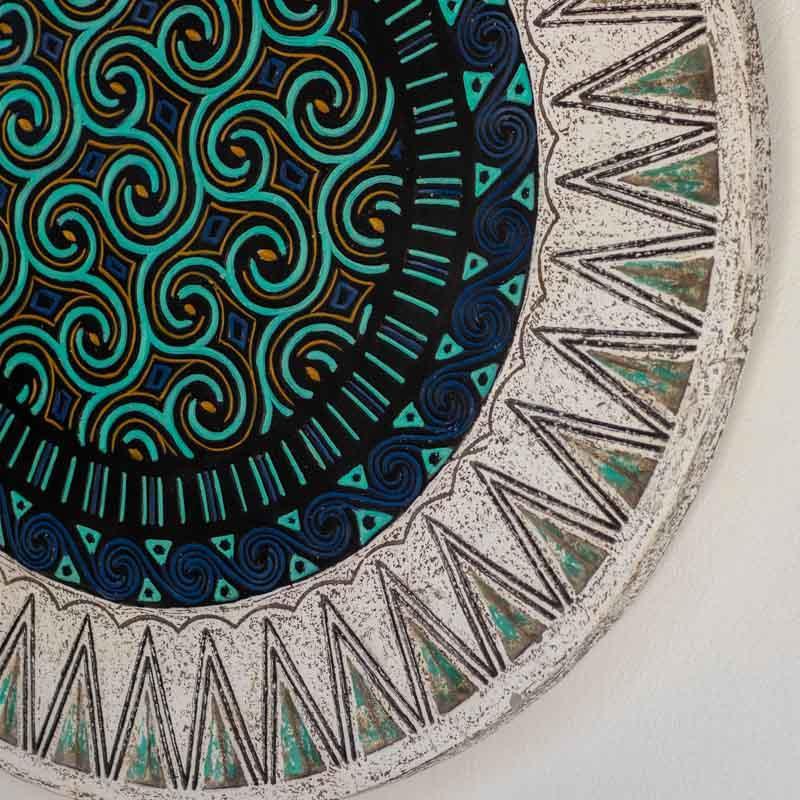 Mandala étnica artesanal de Timor em fibrocimento com padrões geométricos e espirais em azul e preto.