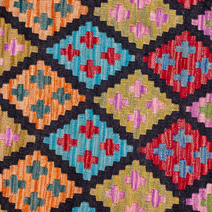 Detalhe da trama têxtil de tapete afegão, destacando a repetição de figuras de diamantes multicoloridos em tons vibrantes e terrosos.