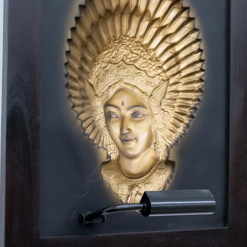 Quadro tridimensional com a deusa Dewi em dourado, destacando-se contra o fundo escuro com iluminação frontal embutida na base.