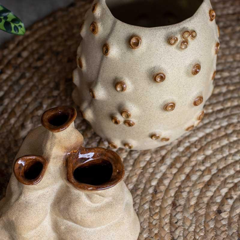 Vaso decorativo artesanal com acabamento fosco e detalhes em relevo orgânico posicionado sobre móvel de madeira.