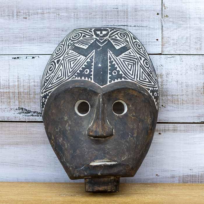 Máscara decorativa esculpida à mão em madeira natural da Ilha de Timor, apresentando detalhes de entalhe profundo e feições ancestrais expressivas.