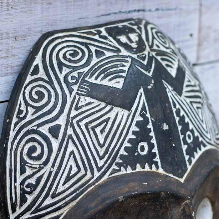 Close-up lateral de máscara artesanal de Timor destacando a textura orgânica da madeira e o acabamento rústico esculpido por artesãos locais.