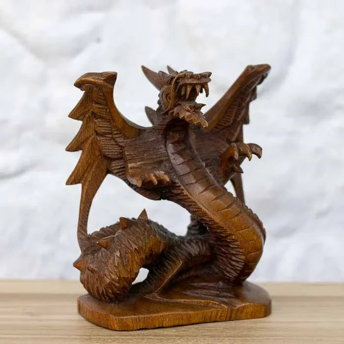 Escultura artesanal de dragão alado em madeira Suar maciça entalhada sobre mesa com livros ao fundo.