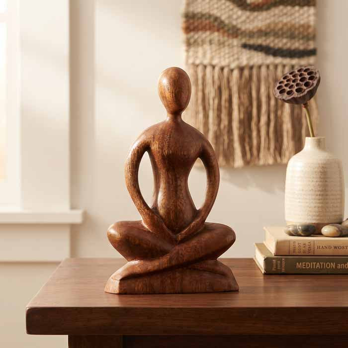 Escultura artesanal de yogi em meditação na posição de lótus esculpida em madeira de Teca maciça sobre mesa.