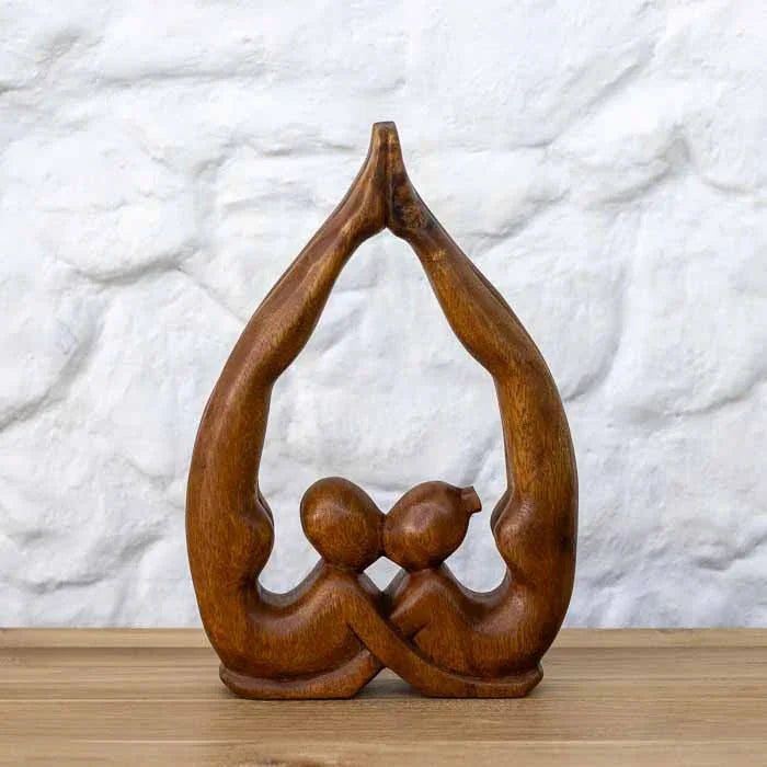 Escultura artesanal abstrata de casal zen em madeira de Teca maciça formando formato de coração sobre mesa.