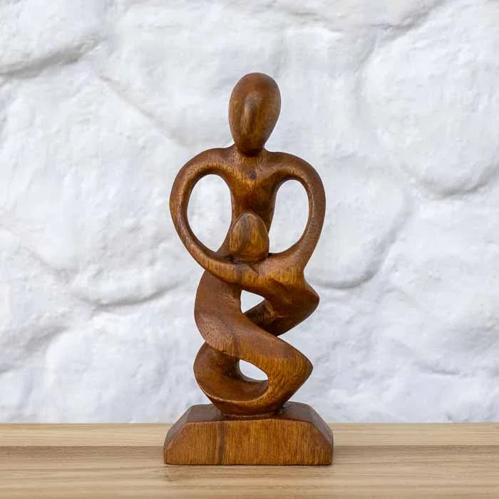 Escultura artesanal abstrata do Amor Paterno em madeira de Teca maciça representando pai e filho sobre mesa.