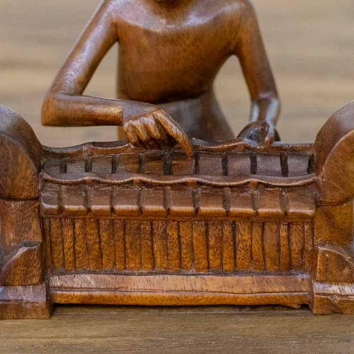 Estatueta decorativo de arte balinesa com figura masculina concentrada na execução musical de Saron. 