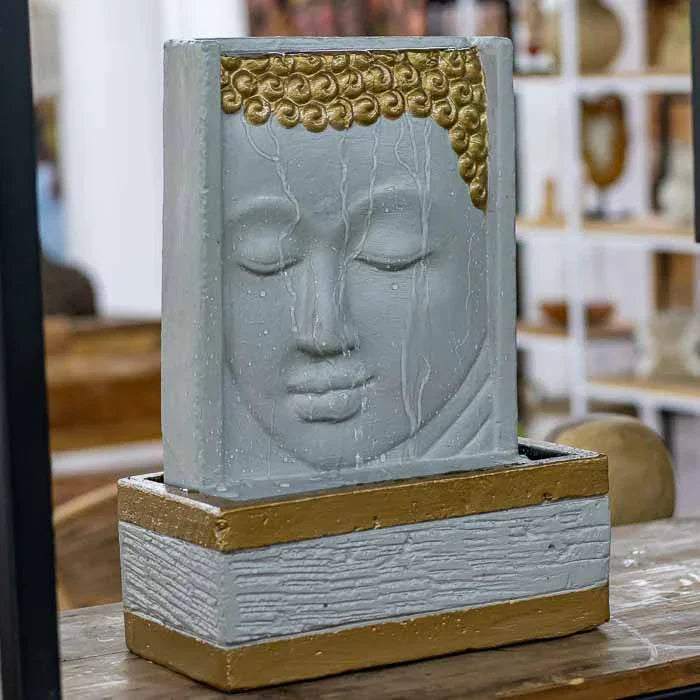 Fonte artesanal em estilo zen, paredão com rosto de Buda em relevo e água corrente. 