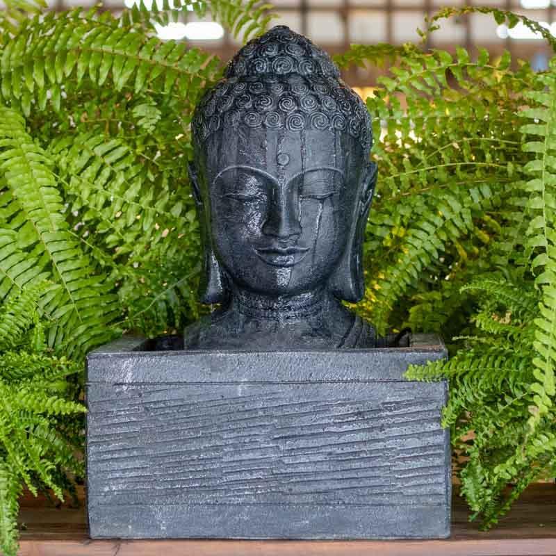 Fonte de água em formato de cabeça de Buda esculpida em cimento preto com fluxo de água superior.