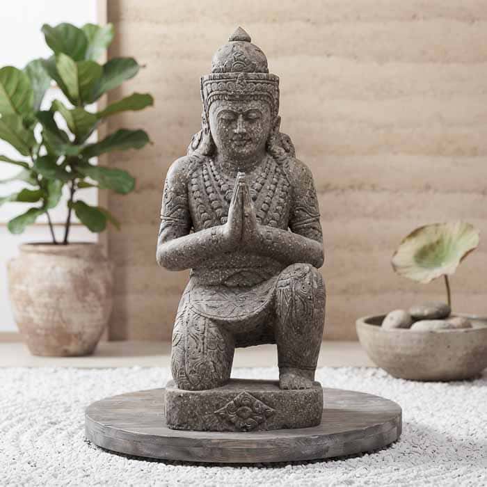 Escultura Buda Namastê entalhada em pedra natural, feita à mão em Bali com acabamento artesanal.