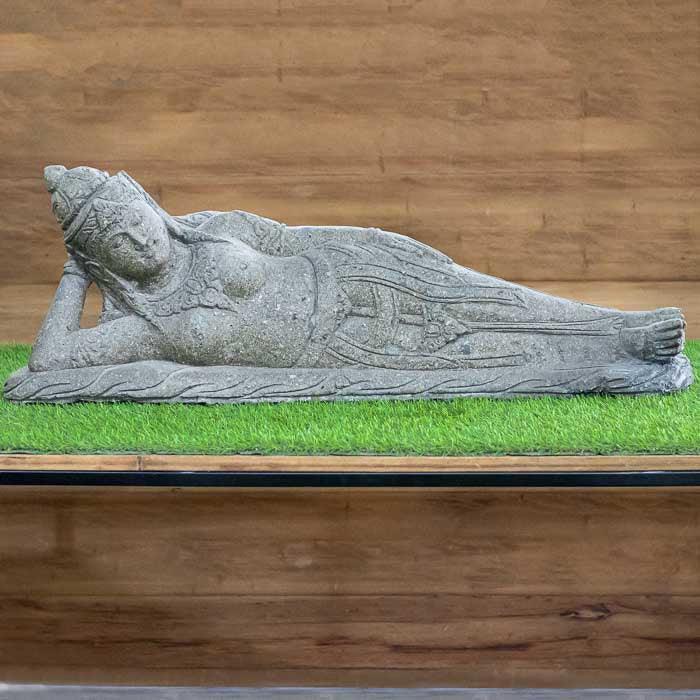 Escultura de Dewi deitada esculpida em pedra natural, com traços suaves e expressão serena típica da arte asiática