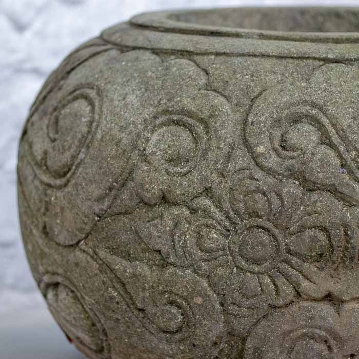 Vaso de paisagismo robusto em pedra vulcânica sobre piso de cimento em área externa.