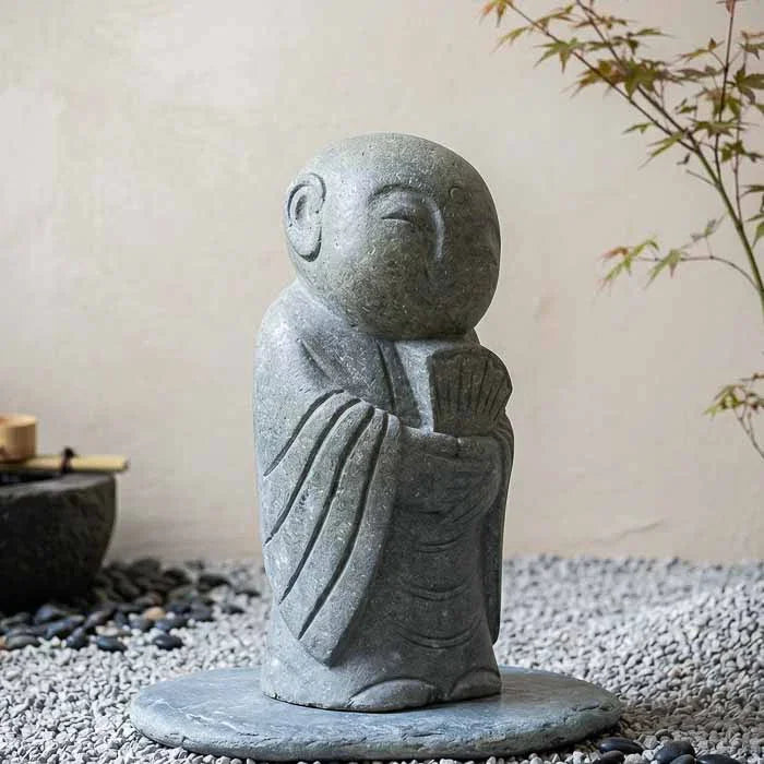 Escultura zen de monge segurando um leque com expressão de alegria e paz interior. 