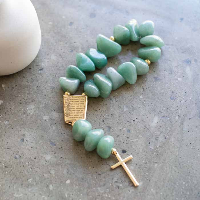 Adorno de mesa sacro em pedras naturais verde e detalhes dourados ao lado de vaso artesanal branco.
